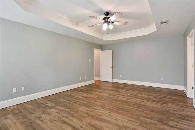 empty room with a raised ceiling, ceiling fan, wood finished floors, baseboards, and ornamental molding