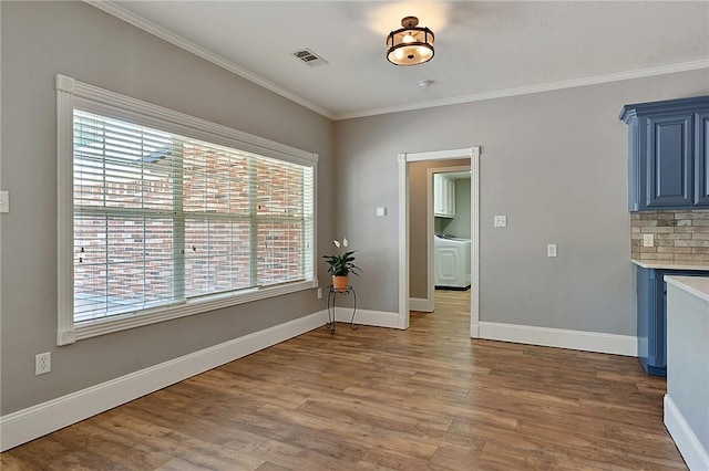 unfurnished dining area with wood finished floors, crown molding, baseboards, and washer / dryer
