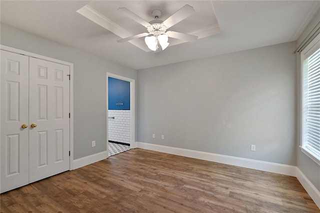 unfurnished bedroom with multiple windows, wood finished floors, and a tray ceiling