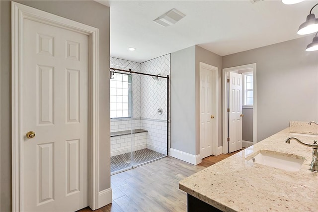 full bath with a shower stall, wood finished floors, baseboards, and double vanity