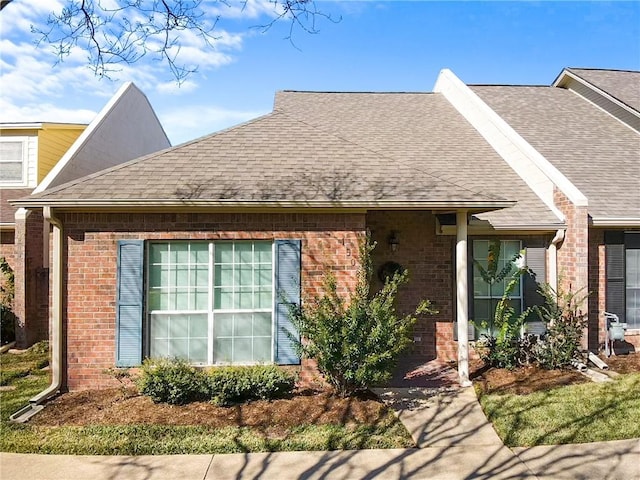 ranch-style house featuring brick siding and roof with shingles