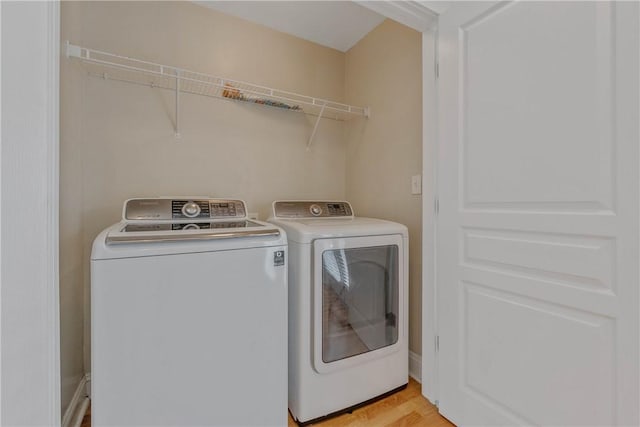 clothes washing area with washing machine and dryer and light wood-type flooring