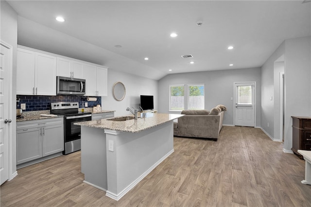 1147 Buffalograss Trl, Sealy, TX 77474 - kitchen featuring stainless steel appliances, a sink, light wood-style floors, light stone countertops, and a center island with sink
