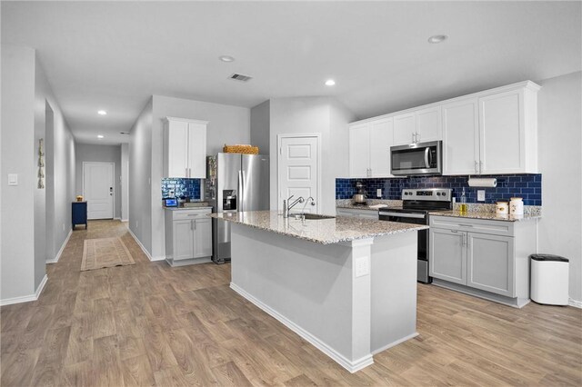 1147 Buffalograss Trl, Sealy, TX 77474 - kitchen featuring appliances with stainless steel finishes, a sink, backsplash, light wood-style floors, and a kitchen island with sink