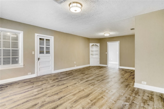 spare room with visible vents, a textured ceiling, baseboards, and wood finished floors