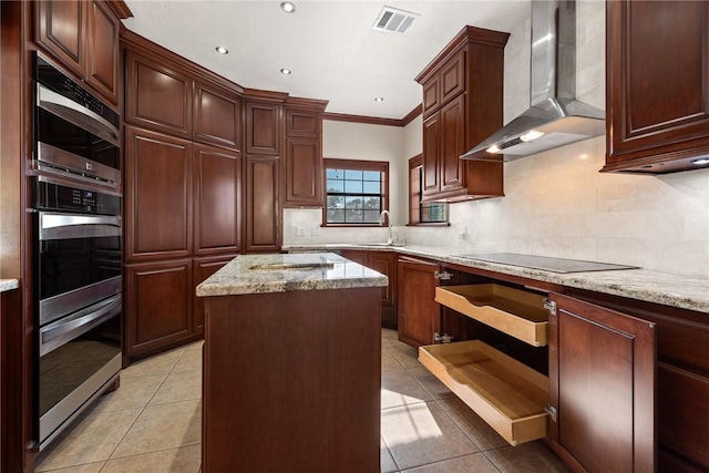 kitchen featuring sink, wall chimney range hood, light tile patterned floors, black electric cooktop, and a kitchen island