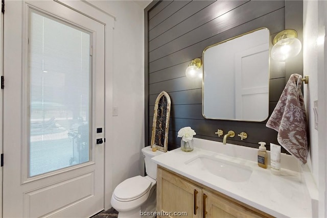 bathroom with wooden walls, vanity, and toilet