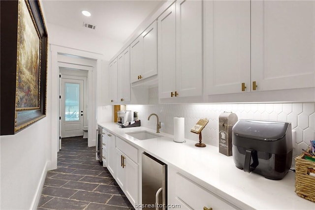 kitchen with decorative backsplash, white cabinetry, beverage cooler, and sink