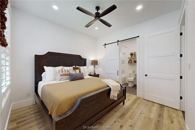 bedroom with ceiling fan, a barn door, light wood-type flooring, and ensuite bath