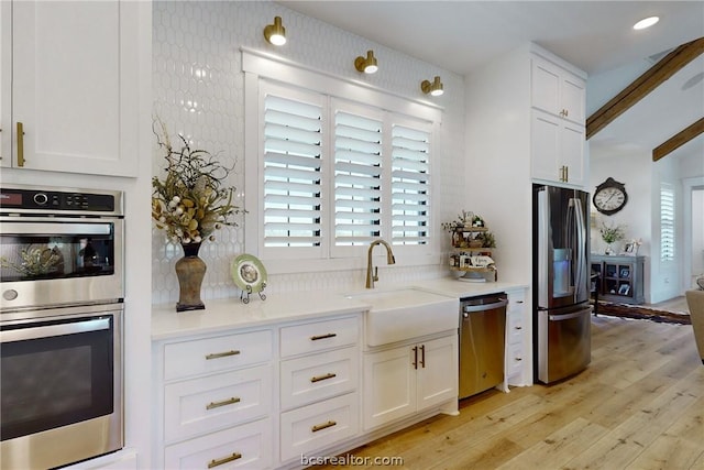 kitchen with appliances with stainless steel finishes, sink, beam ceiling, light hardwood / wood-style flooring, and white cabinetry