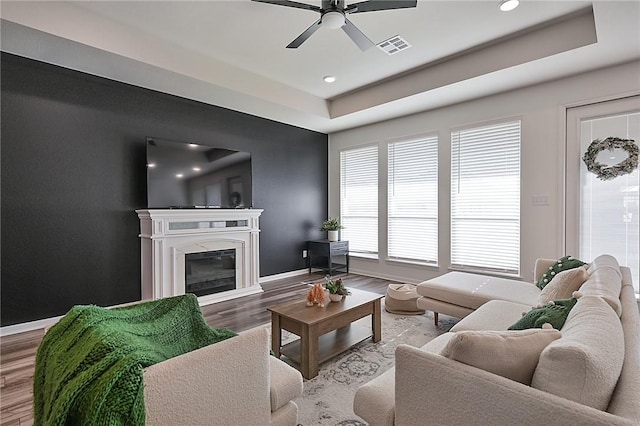 living room with hardwood / wood-style floors, a tray ceiling, and ceiling fan