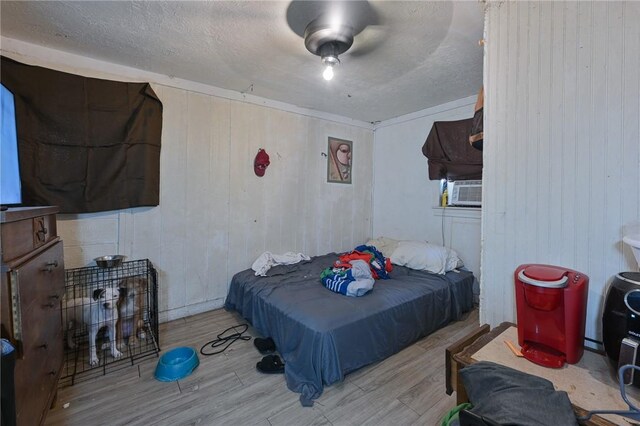 bedroom with a textured ceiling, cooling unit, and wood finished floors