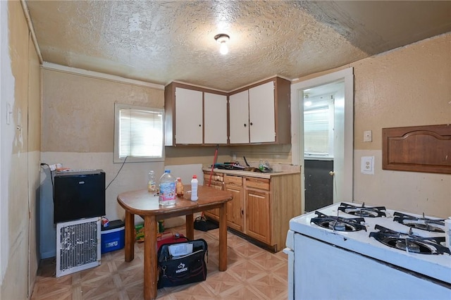 kitchen with a textured ceiling, white cabinets, white range with gas cooktop, light countertops, and light floors