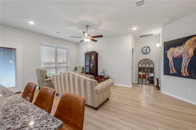 living room featuring visible vents, a ceiling fan, baseboards, and light wood-type flooring