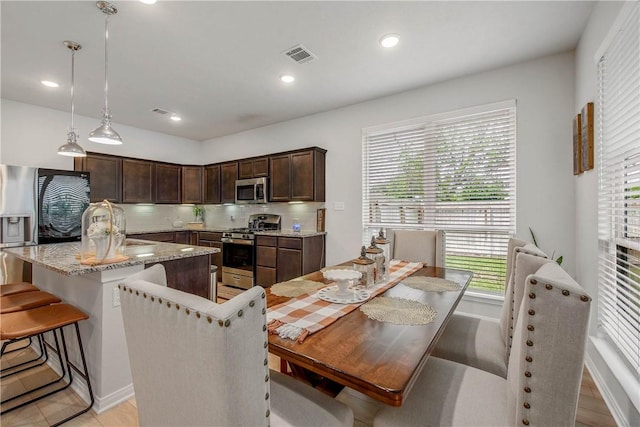 kitchen featuring dark brown cabinetry, hanging light fixtures, appliances with stainless steel finishes, tasteful backsplash, and visible vents