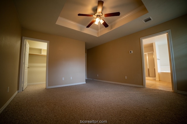 unfurnished bedroom featuring a spacious closet, light colored carpet, a raised ceiling, and ceiling fan