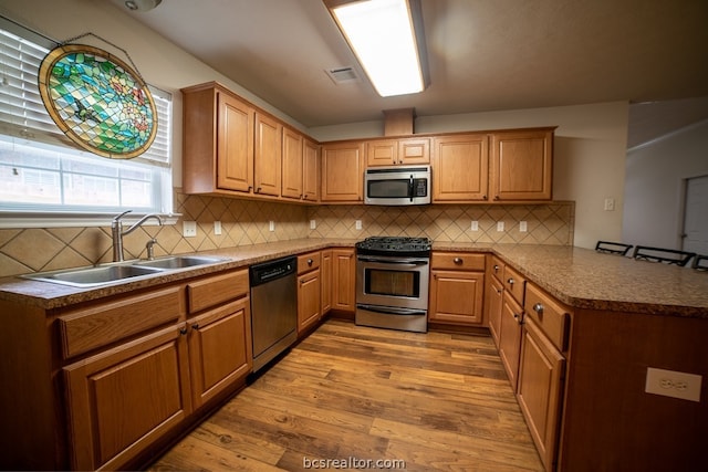 kitchen with decorative backsplash, appliances with stainless steel finishes, light hardwood / wood-style floors, and sink