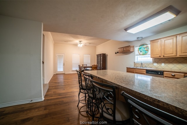 kitchen featuring dishwasher, light brown cabinets, a breakfast bar, dark wood-type flooring, and tasteful backsplash