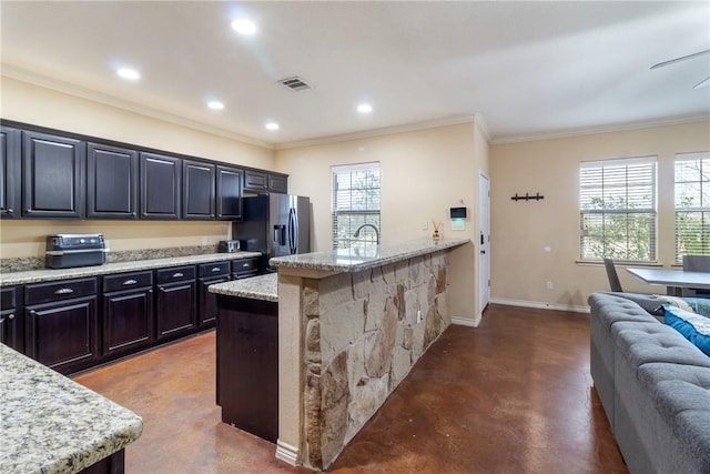 kitchen with light stone countertops, an island with sink, stainless steel fridge, and concrete flooring