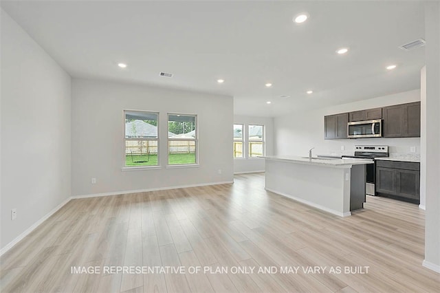 kitchen featuring dark brown cabinetry, light hardwood / wood-style flooring, an island with sink, stainless steel appliances, and light stone counters