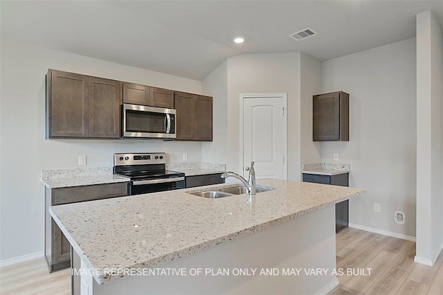 kitchen with vaulted ceiling, sink, a kitchen island with sink, stainless steel appliances, and light stone counters