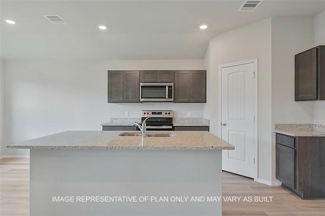 kitchen with stainless steel appliances, sink, dark brown cabinetry, and a kitchen island with sink