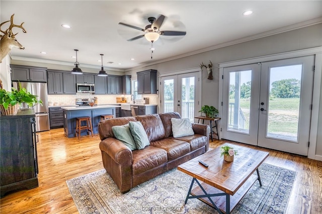 living room with french doors, light wood-type flooring, ornamental molding, and sink