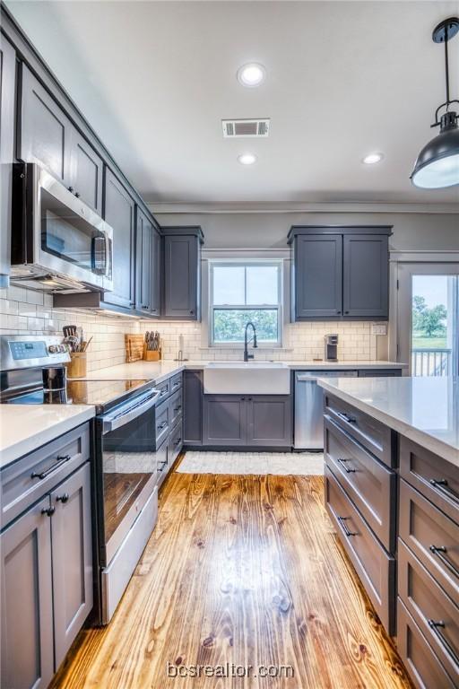 kitchen with backsplash, stainless steel appliances, sink, decorative light fixtures, and light hardwood / wood-style floors