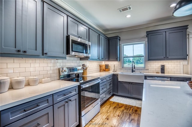 kitchen with sink, tasteful backsplash, light hardwood / wood-style flooring, crown molding, and appliances with stainless steel finishes