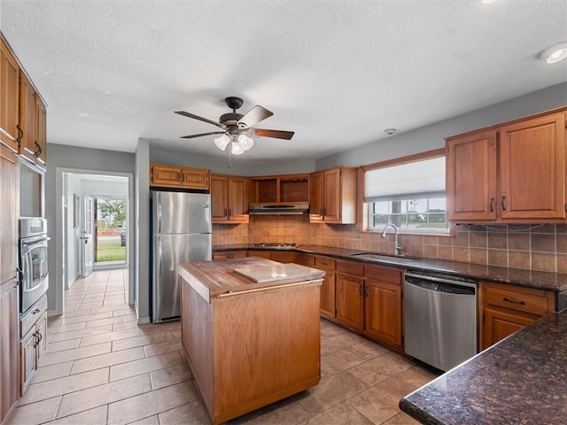 17645 Hwy 6, Navasota, TX 77868 - kitchen with stainless steel appliances, under cabinet range hood, a kitchen island, decorative backsplash, and a textured ceiling