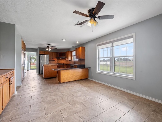 17645 Hwy 6, Navasota, TX 77868 - kitchen with ceiling fan, backsplash, freestanding refrigerator, brown cabinetry, and under cabinet range hood