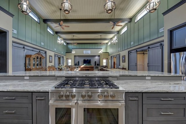 kitchen with stainless steel appliances, a barn door, light stone counters, and beamed ceiling