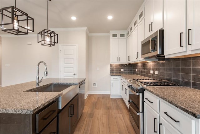 kitchen featuring appliances with stainless steel finishes, a center island with sink, white cabinetry, and pendant lighting