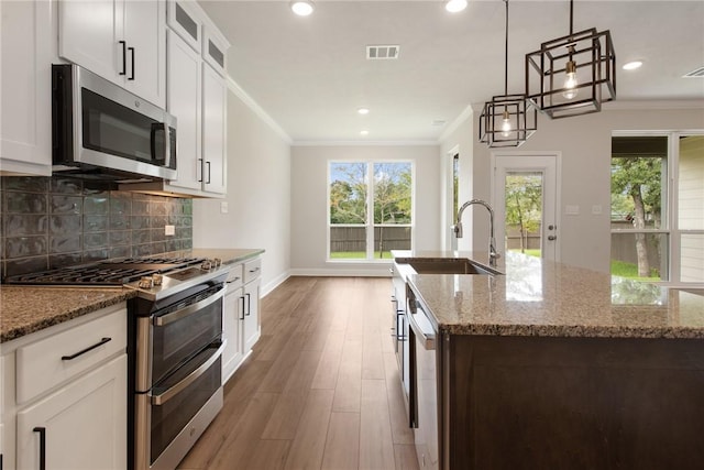 kitchen with appliances with stainless steel finishes, a kitchen island with sink, wood-type flooring, white cabinets, and hanging light fixtures