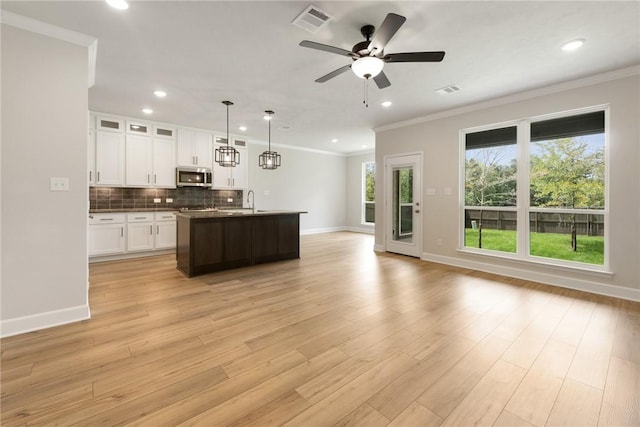 kitchen with white cabinets, light hardwood / wood-style flooring, ceiling fan, an island with sink, and decorative light fixtures