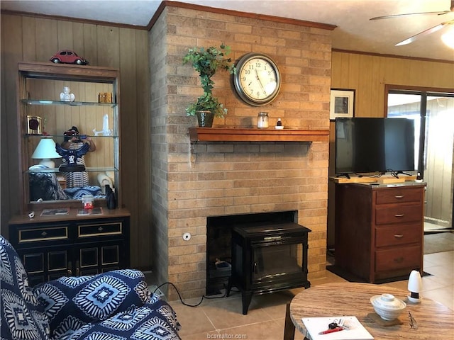 living room featuring light tile patterned flooring, wooden walls, a ceiling fan, a wood stove, and crown molding