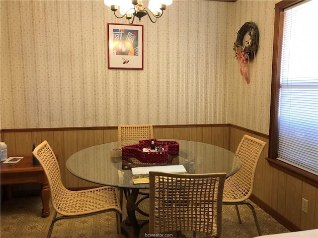 dining area with wainscoting, wood walls, an inviting chandelier, and wallpapered walls