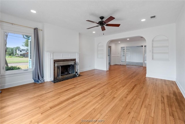 unfurnished living room with built in shelves, ceiling fan, light hardwood / wood-style floors, and a tile fireplace