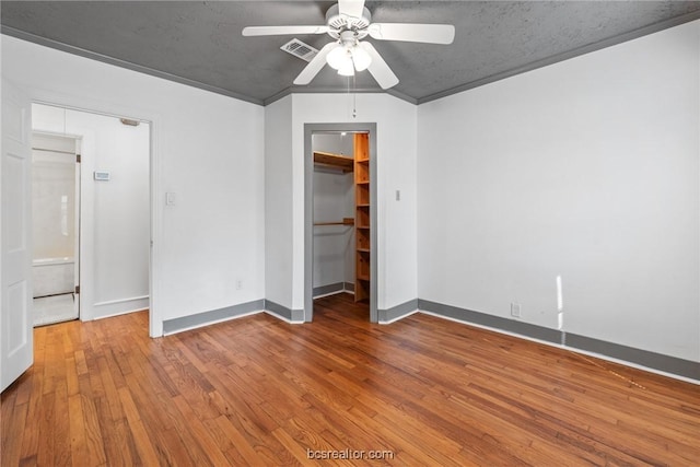 unfurnished bedroom featuring a walk in closet, ornamental molding, ceiling fan, hardwood / wood-style floors, and a closet