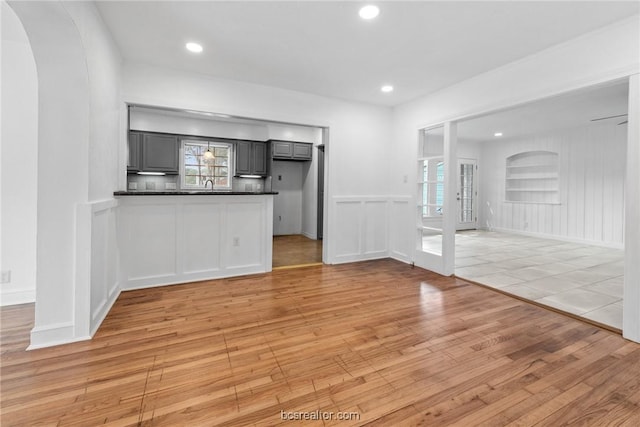 unfurnished living room with built in shelves, light wood-type flooring, sink, and french doors