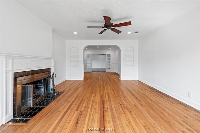 unfurnished living room with a fireplace, ceiling fan, a textured ceiling, and light hardwood / wood-style flooring