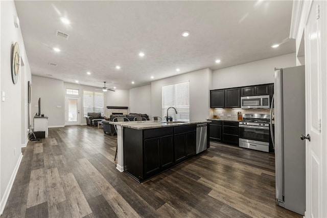 kitchen featuring light stone countertops, dark hardwood / wood-style flooring, stainless steel appliances, and a center island with sink