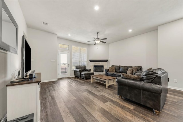 living room with a fireplace, ceiling fan, and dark wood-type flooring