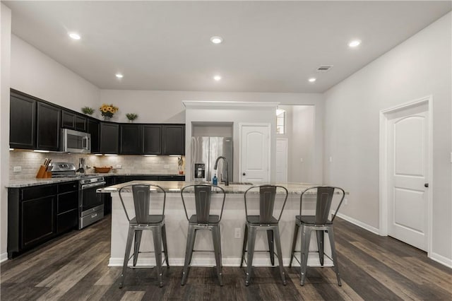 kitchen featuring light stone countertops, a kitchen island with sink, dark wood-type flooring, and appliances with stainless steel finishes