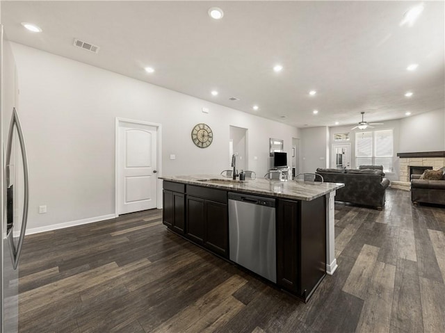 kitchen featuring sink, stainless steel appliances, light stone counters, dark hardwood / wood-style flooring, and a kitchen island with sink