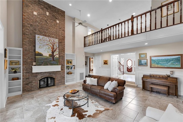 living room with a ceiling fan, a high ceiling, a fireplace, stairway, and built in shelves