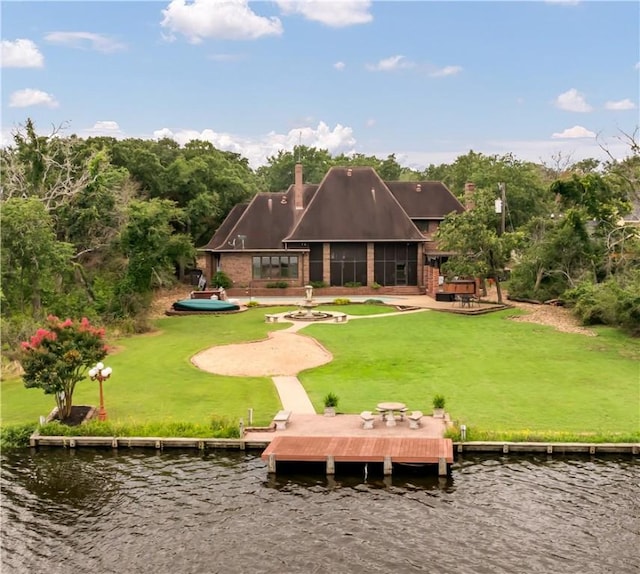 back of house with brick siding, a water view, a chimney, and a lawn