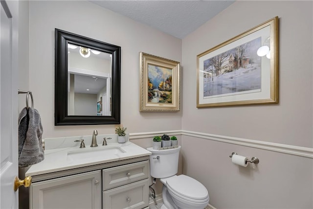 bathroom featuring toilet, baseboards, vanity, and a textured ceiling