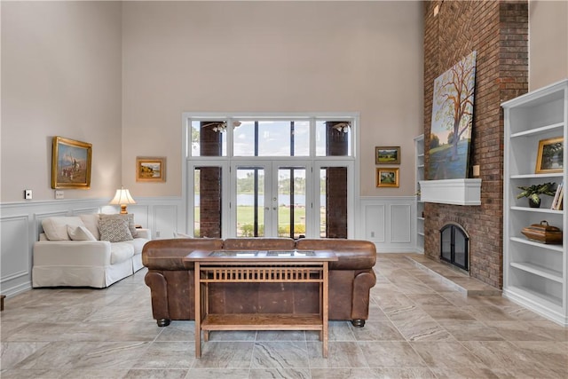 living area featuring french doors, built in features, a decorative wall, a fireplace, and a high ceiling