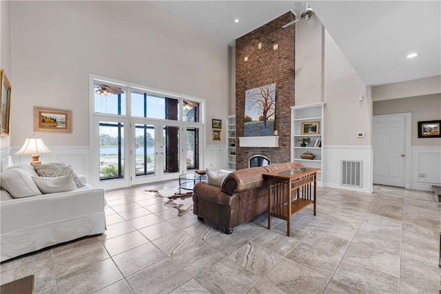 living room featuring a wainscoted wall, a decorative wall, visible vents, and a high ceiling